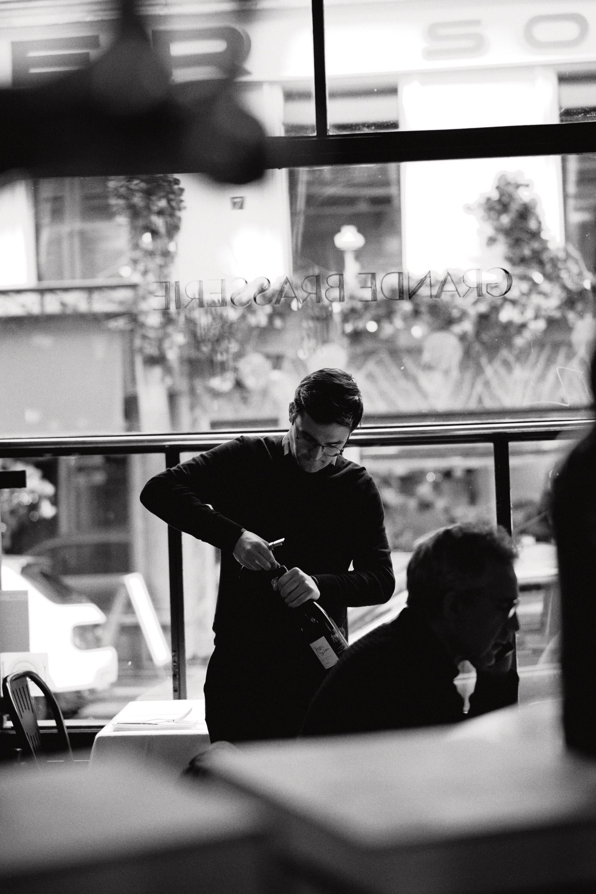 Serveur débouchant une bouteille devant la vitrine, en noir et blanc