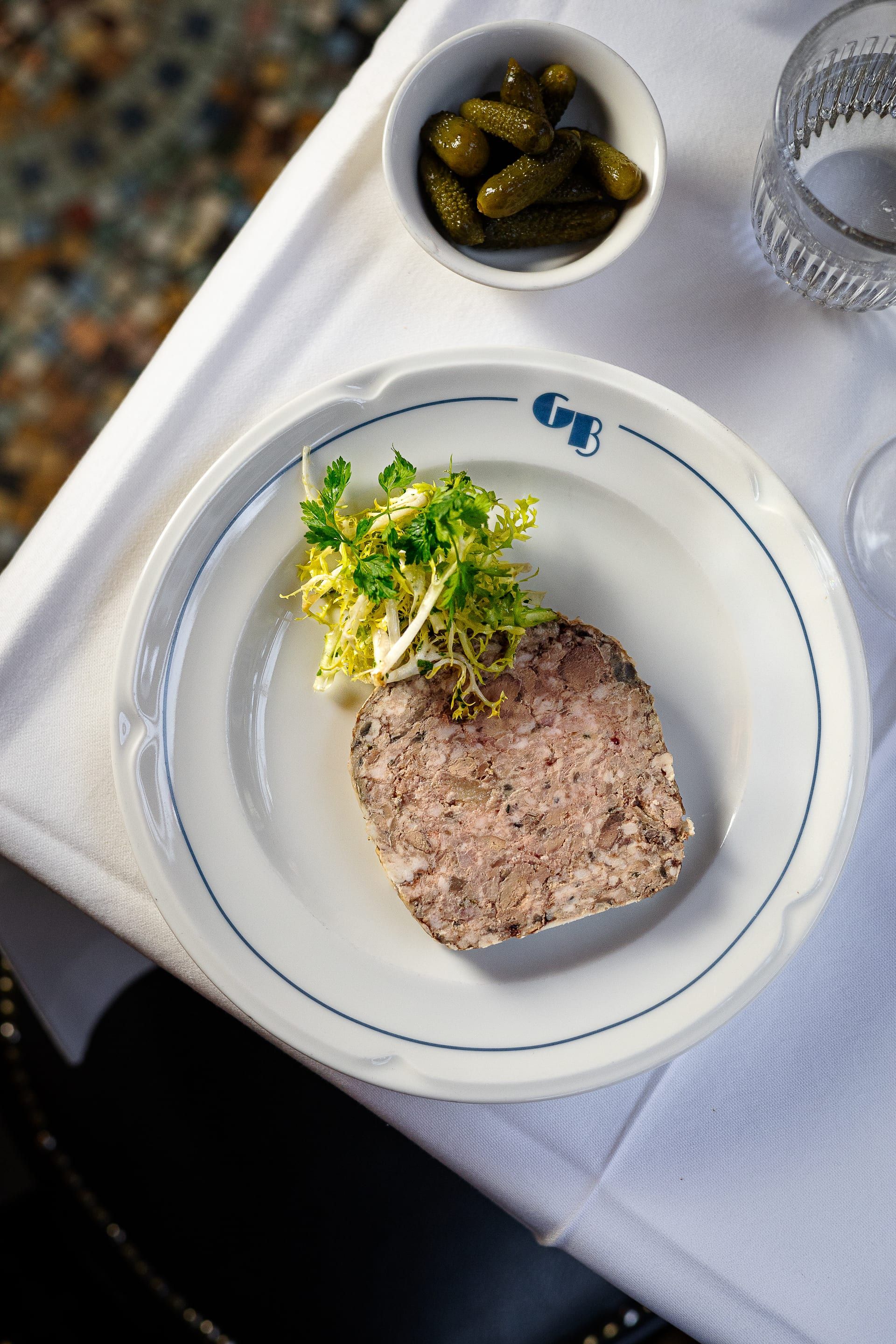 Tranche de pâté, salade frisée et cornichons, sur une assiette au monogramme GB